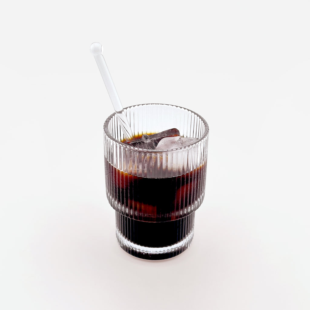 A reeded double-wall glass filled with coffee and a matching glass spoon