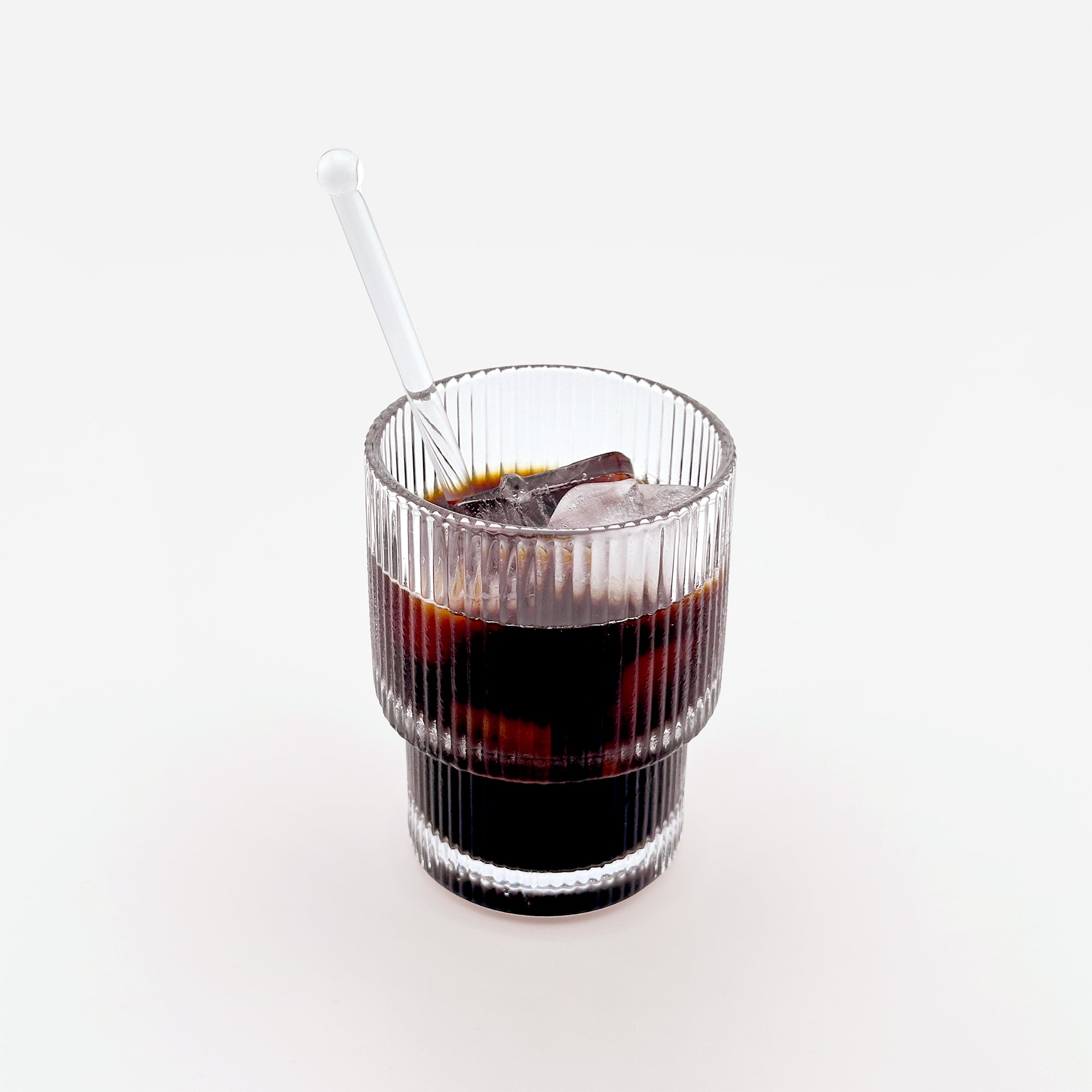 A reeded double-wall glass filled with coffee and a matching glass spoon